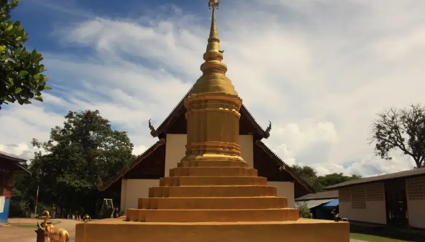 Złota pagoda, symbol buddyzmu, wznosi się na tle błękitnego nieba. Obok stoi złoty słoń.