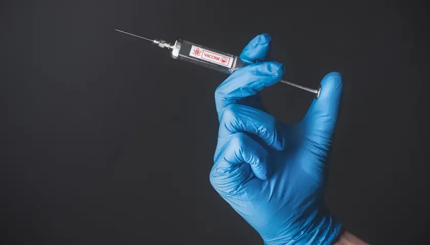 Ręka w niebieskiej rękawiczce trzyma strzykawkę z napisem "VACCINE". To symbol nadziei na bezpieczne podróże, np. do Tunezji, gdzie tunezja szczepienia są ważne.