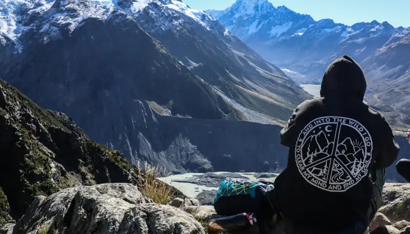 Osoba w bluzie z napisem "Into the Wild" patrzy na najwyższy szczyt Nowej Zelandii, Aoraki/Mount Cook.