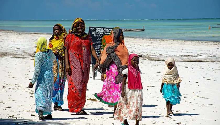 Kobiety i dziewczynki w kolorowych strojach spacerują po plaży Zanzibaru. Myślą o wakacjach i o tym, jakie **szczepienia** są potrzebne.