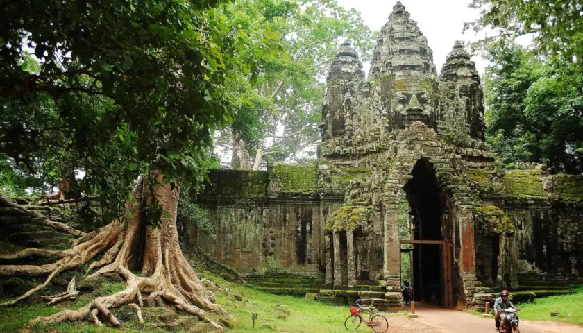 Wspaniałe kamienne twarze Angkor Thom witają na kambodżańskie wakacje. Potężne korzenie drzew oplatają starożytne mury.