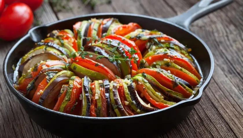Piękne francuskie jedzenie: ratatouille w żeliwnej patelni, z plastrów cukinii, bakłażana i pomidorów, doprawione ziołami.
