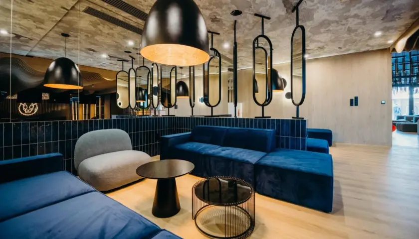 Nowoczesne wnętrze z niebieskimi sofami i szarym fotelem. Stylowe lampy i lustra tworzą atmosferę godną 4-gwiazdkowego hotelu.