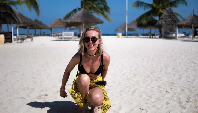 Uśmiechnięta blondynka w bikini i żółtej spódniczce na piaszczystej plaży. Idealne zanzibar wakacje pod palmami.