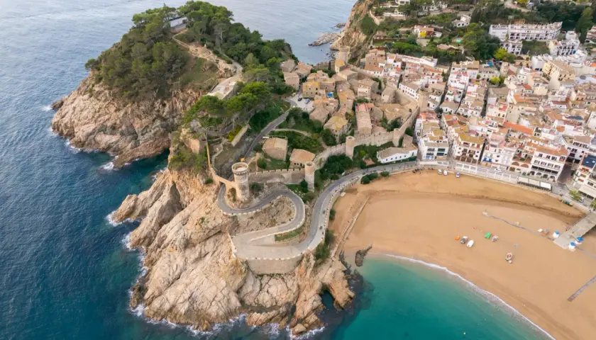 Malownicze widoki na Costa Brava wakacje: miasteczko z zamkiem na klifie, kręta droga i piaszczysta plaża.
