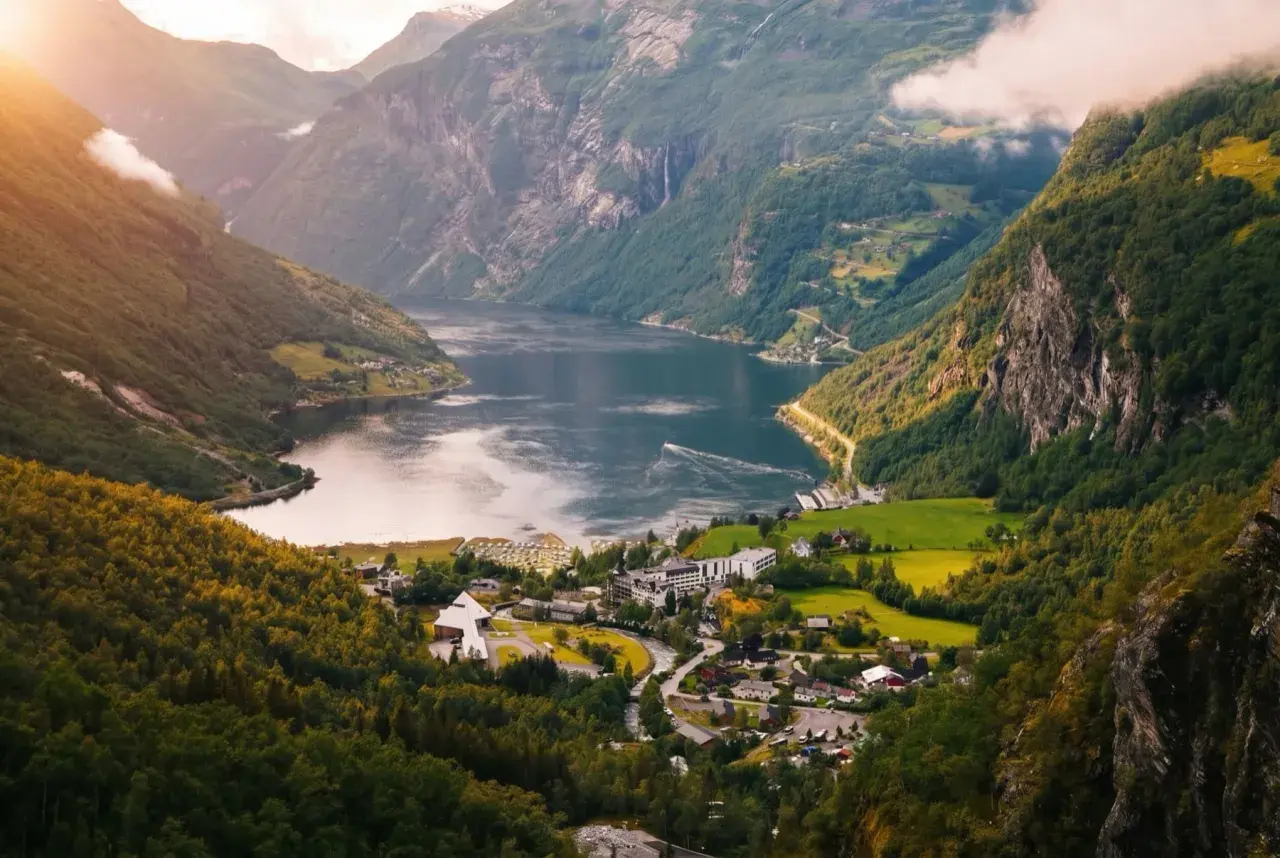 Widok na malownicze fiordy norweskie z górami, jeziorem i małą wioską. Słońce przebija się przez chmury.