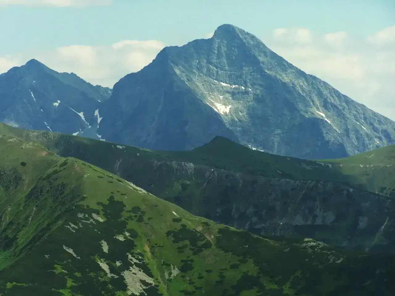 Majestatyczny szczyt w Tatrach Wysokich 2494 m, otoczony zielonymi grzbietami i skalistymi zboczami, z resztkami śniegu.