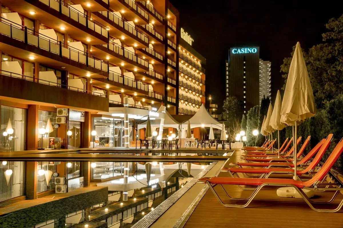 Hotel Gladiola Star nocą, z basenem, leżakami i kasynem w tle.