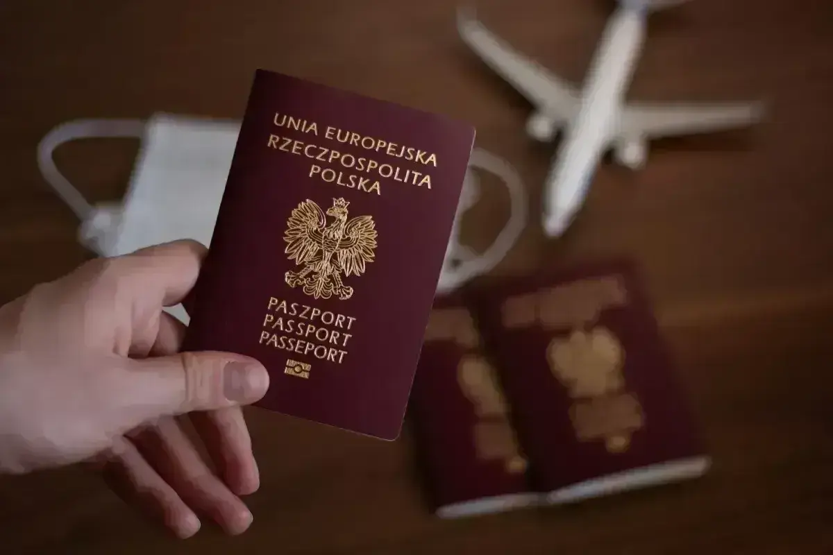 Dłoń trzyma polski paszport. Obok leżą kolejne dokumenty, maseczka i samolot. Czy do Anglii potrzebny jest paszport? Tak, jest niezbędny.