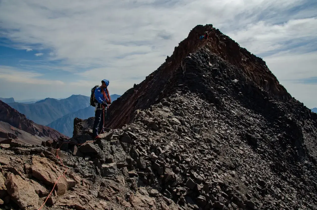 Alpinista na grani, zbliża się do najwyższego szczytu Gruzji. W tle górzyste krajobrazy.