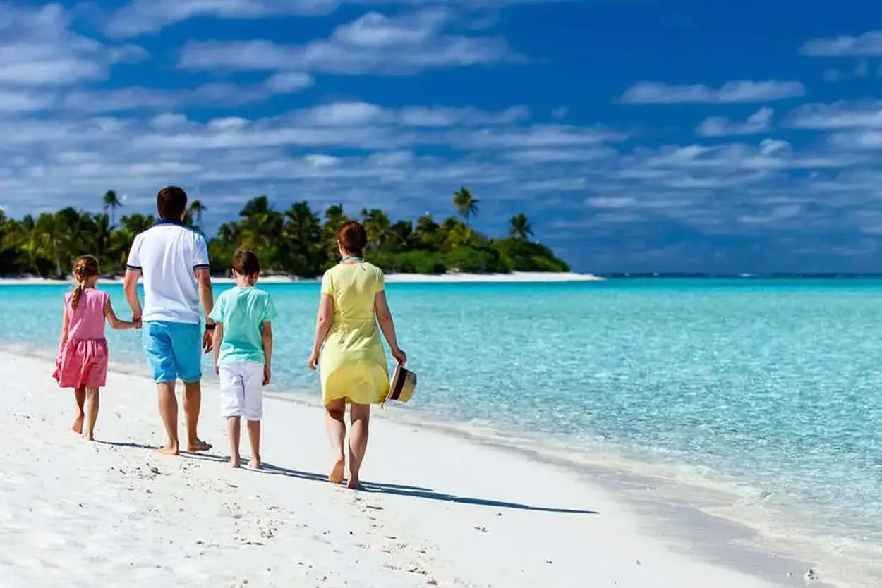 Rodzina cieszy się wakacjami z dziećmi za granicą, spacerując po rajskiej plaży z turkusową wodą i palmami w tle.