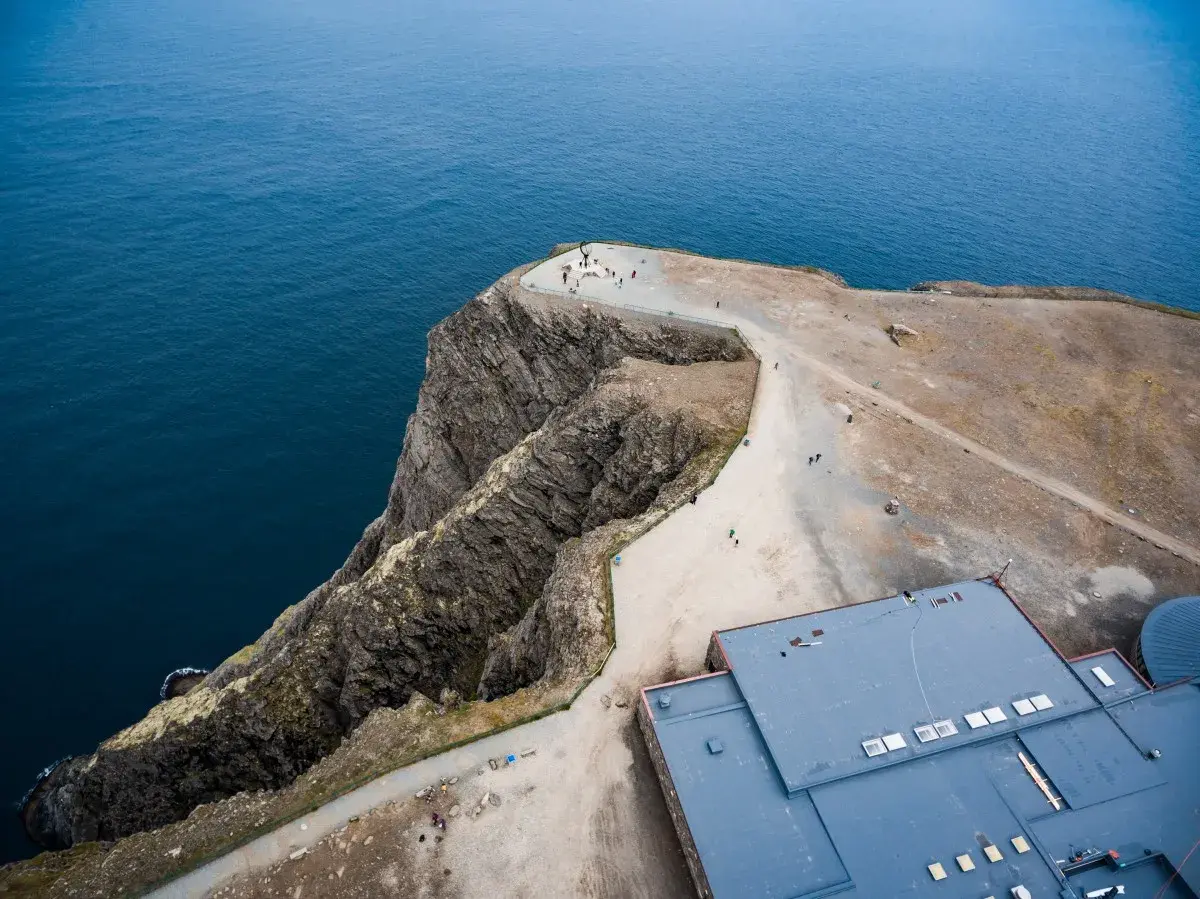 Widok z lotu ptaka na klifowe wybrzeże i budynek przy Nordkapp. Turyści podziwiają ocean.