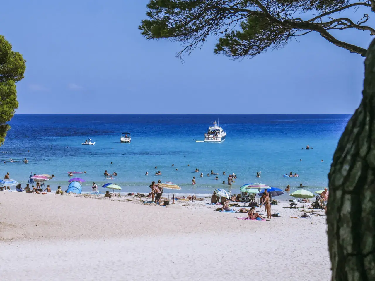 Słoneczna plaża na Balearach, ludzie opalają się i kąpią w turkusowym morzu.