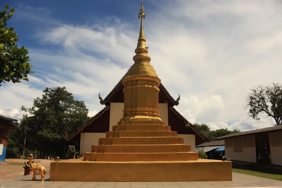 Złota pagoda, symbol buddyzmu, wznosi się na tle błękitnego nieba. Obok stoi złoty słoń.