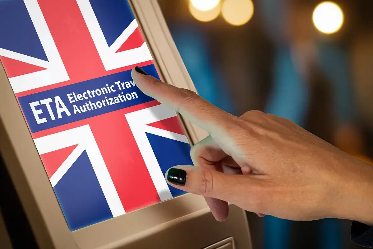 Dłoń dotyka ekranu z flagą Wielkiej Brytanii i napisem ETA. Czy Polacy potrzebują wizy do Wielkiej Brytanii? ETA to elektroniczne zezwolenie na podróż.