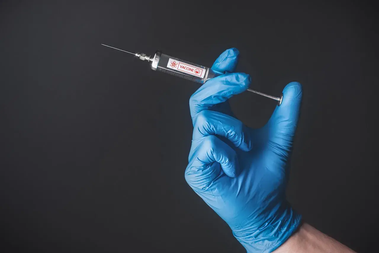 Ręka w niebieskiej rękawiczce trzyma strzykawkę z napisem "VACCINE". To symbol nadziei na bezpieczne podróże, np. do Tunezji, gdzie tunezja szczepienia są ważne.