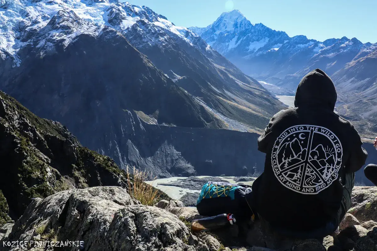 Osoba w bluzie z napisem "Into the Wild" patrzy na najwyższy szczyt Nowej Zelandii, Aoraki/Mount Cook.