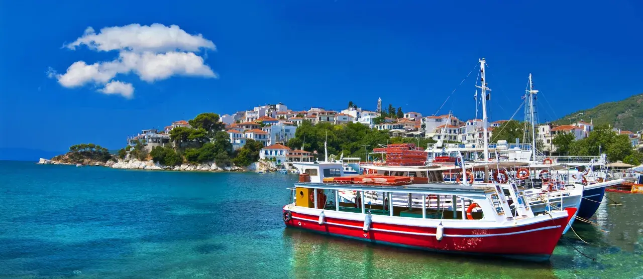 Skopelos wakacje: białe domy na wzgórzu, turkusowa woda i łodzie w porcie. Idealne miejsce na greckie wakacje.