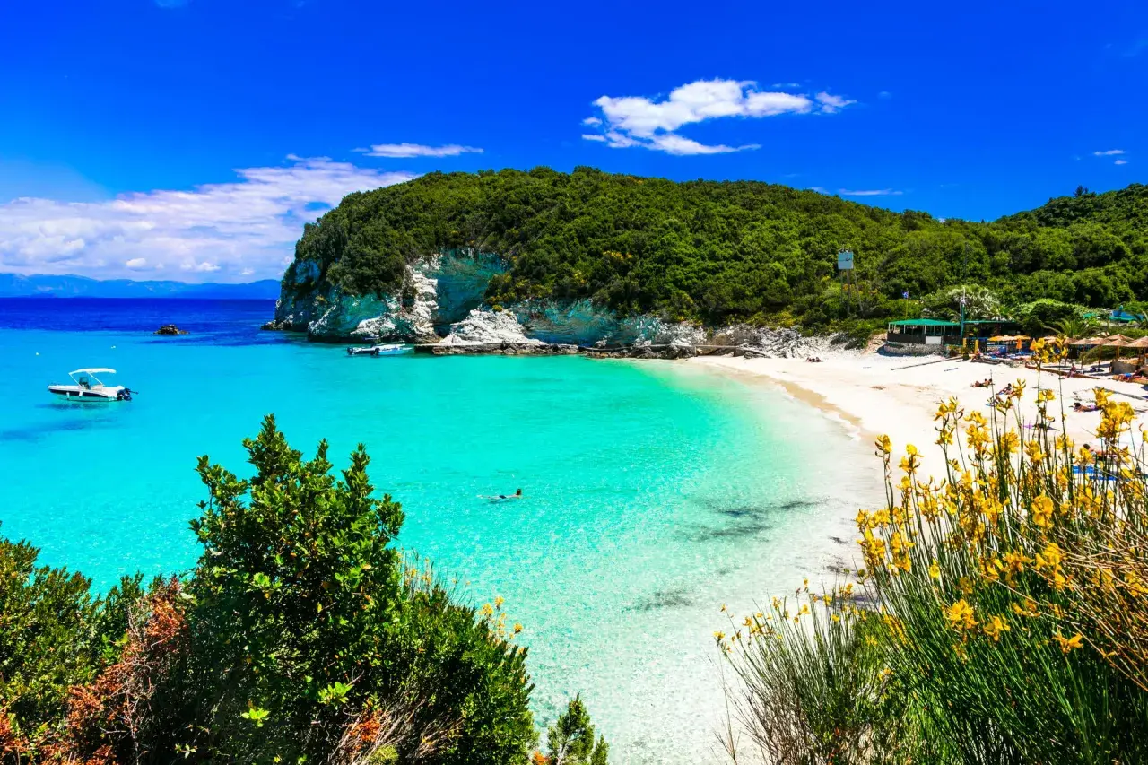Rajska plaża na Paxos i Antipaxos. Turkusowa woda, biały piasek, zielone wzgórza i żółte kwiaty tworzą idylliczny krajobraz.