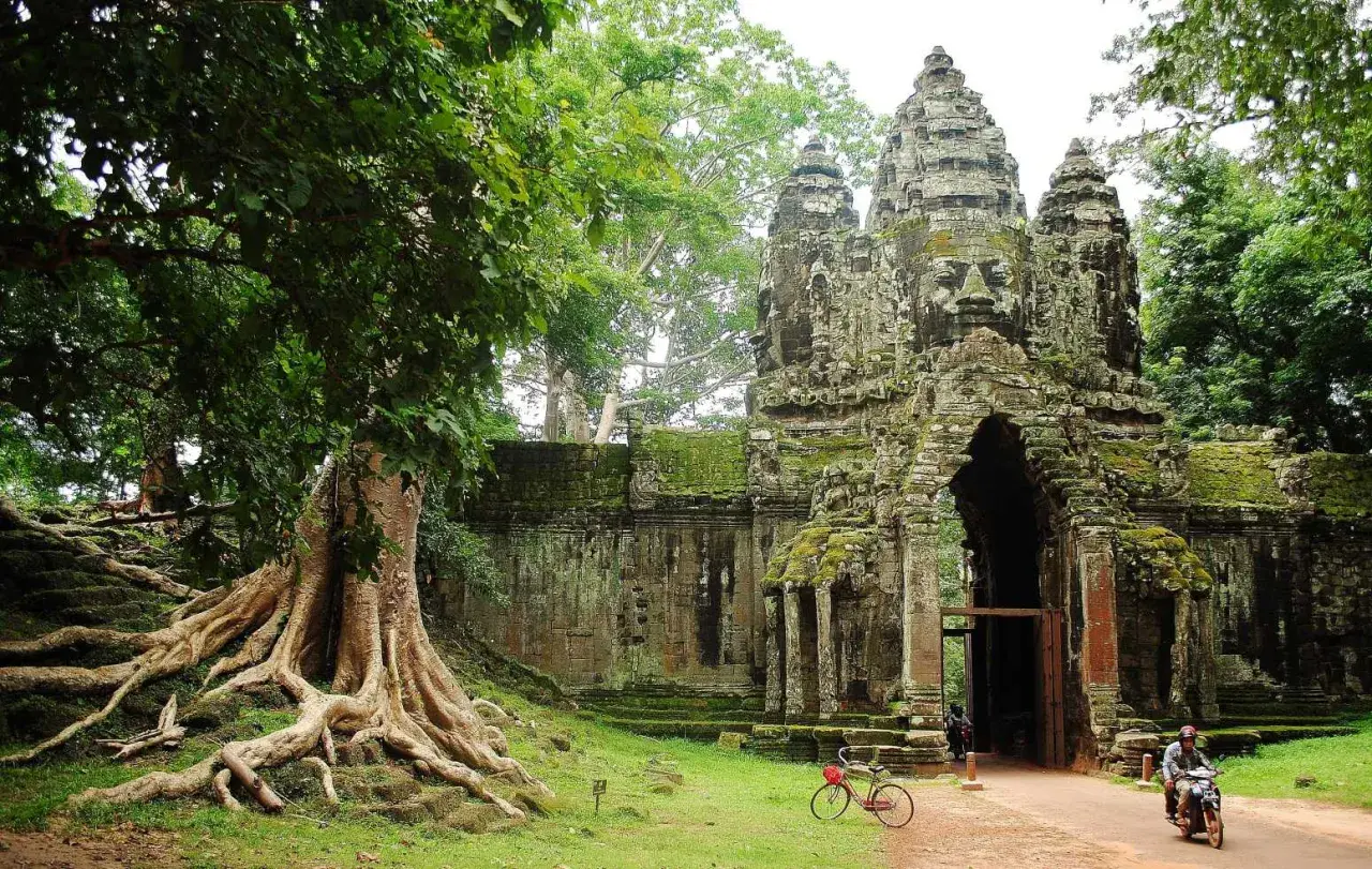 Wspaniałe kamienne twarze Angkor Thom witają na kambodżańskie wakacje. Potężne korzenie drzew oplatają starożytne mury.
