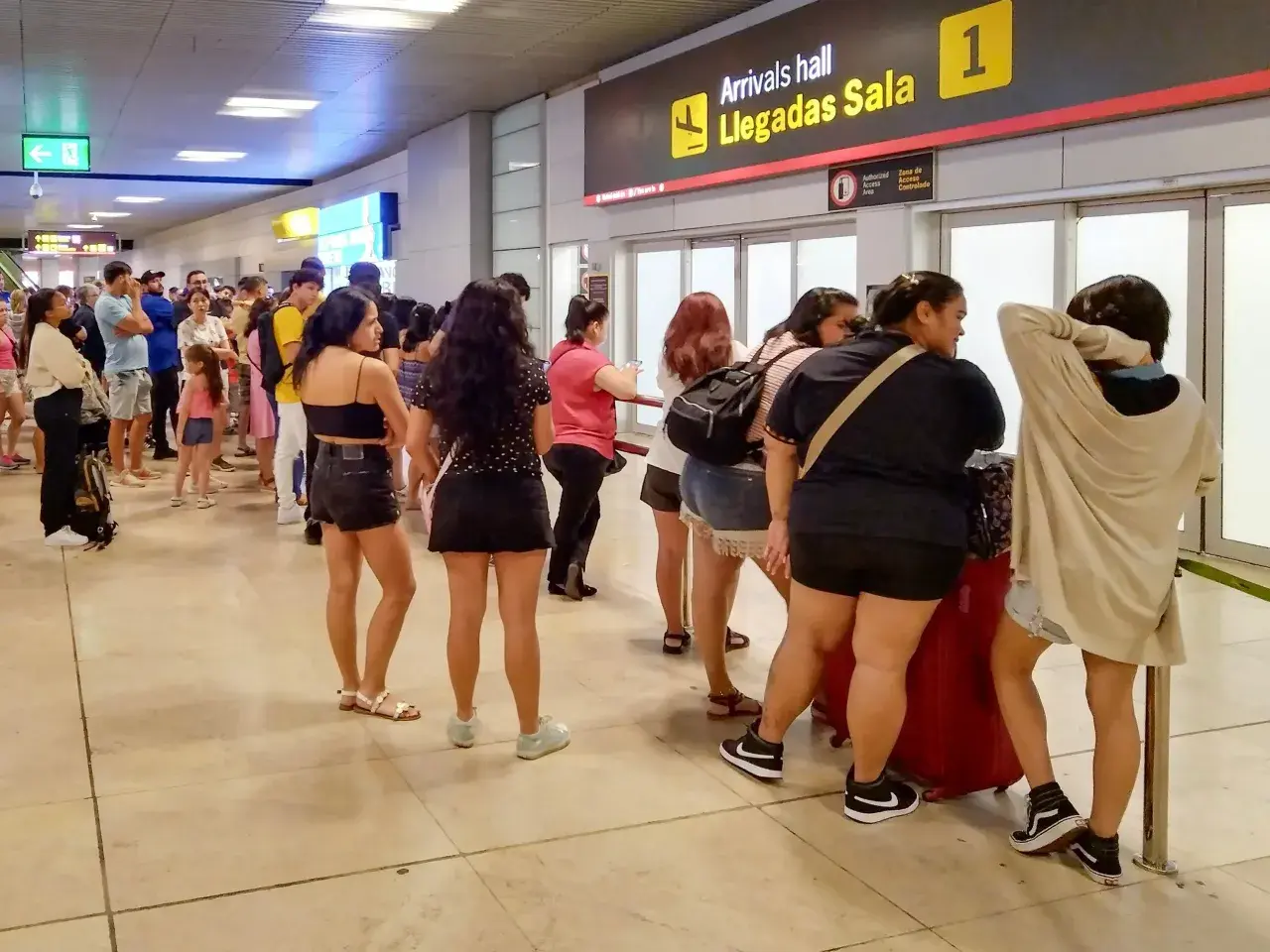 Kolejka podróżnych na lotnisku w Hiszpanii, przy tablicy "Arrivals hall Llegadas Sala 1".
