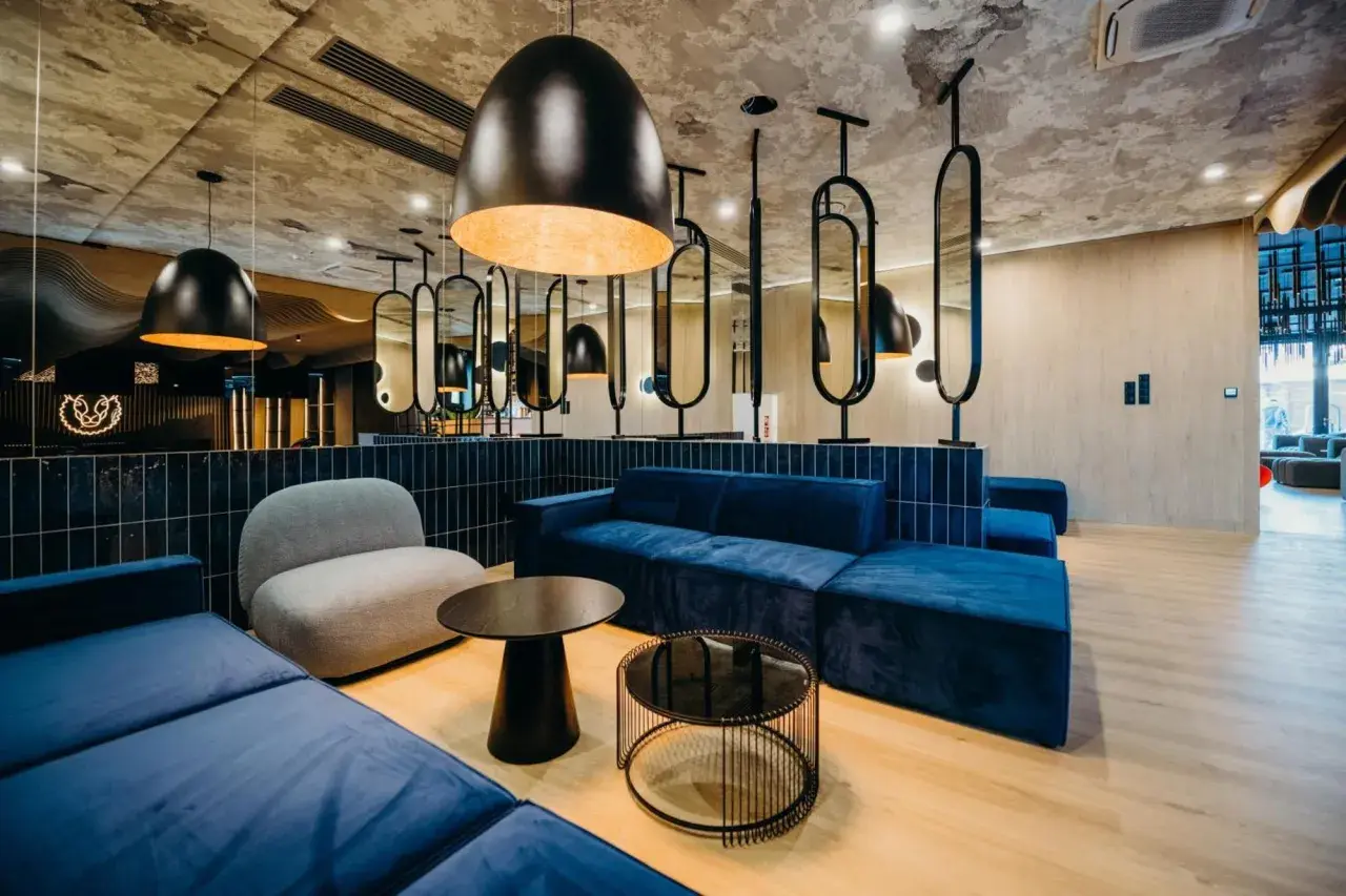 Nowoczesne wnętrze z niebieskimi sofami i szarym fotelem. Stylowe lampy i lustra tworzą atmosferę godną 4-gwiazdkowego hotelu.