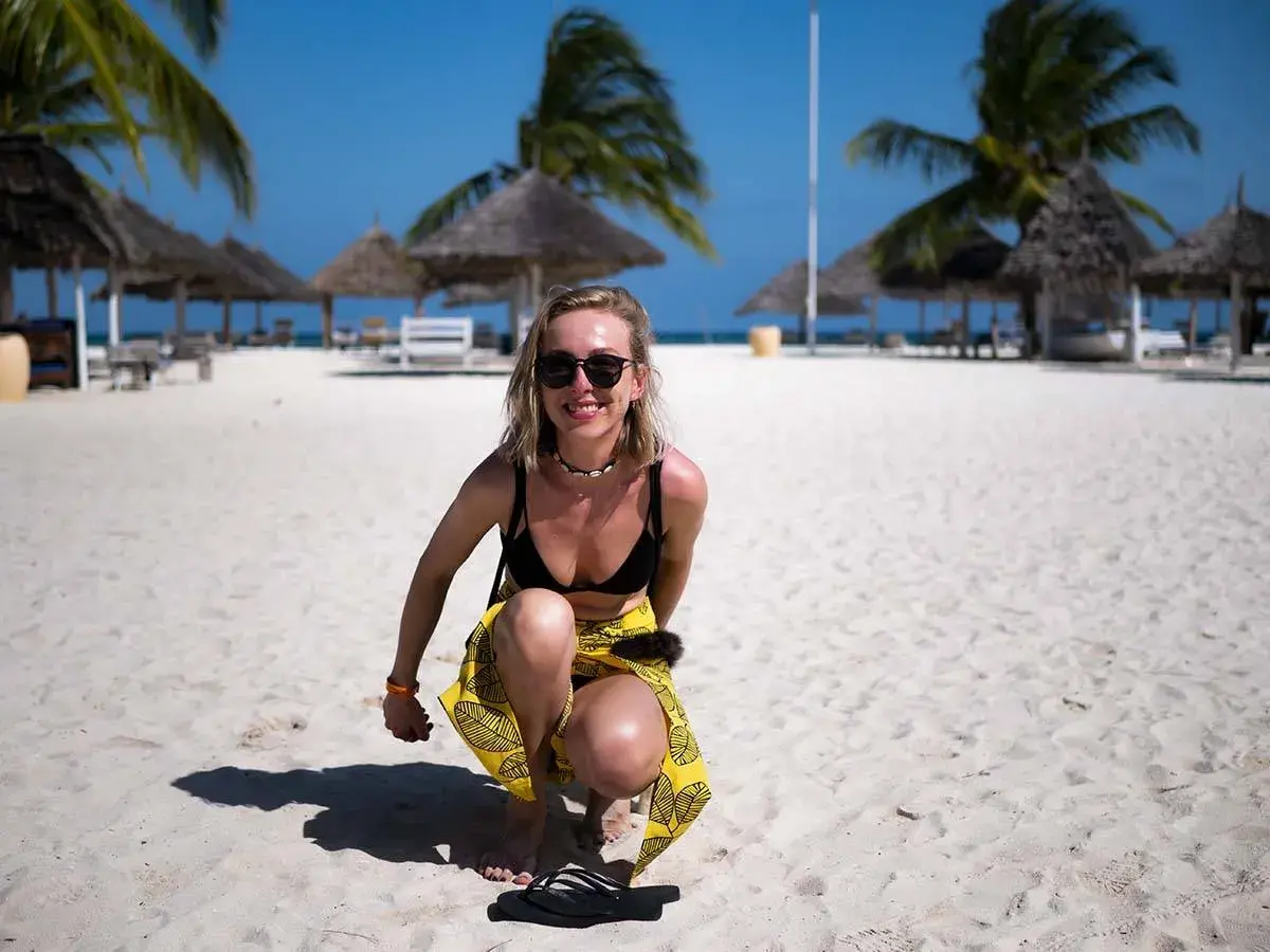 Uśmiechnięta blondynka w bikini i żółtej spódniczce na piaszczystej plaży. Idealne zanzibar wakacje pod palmami.