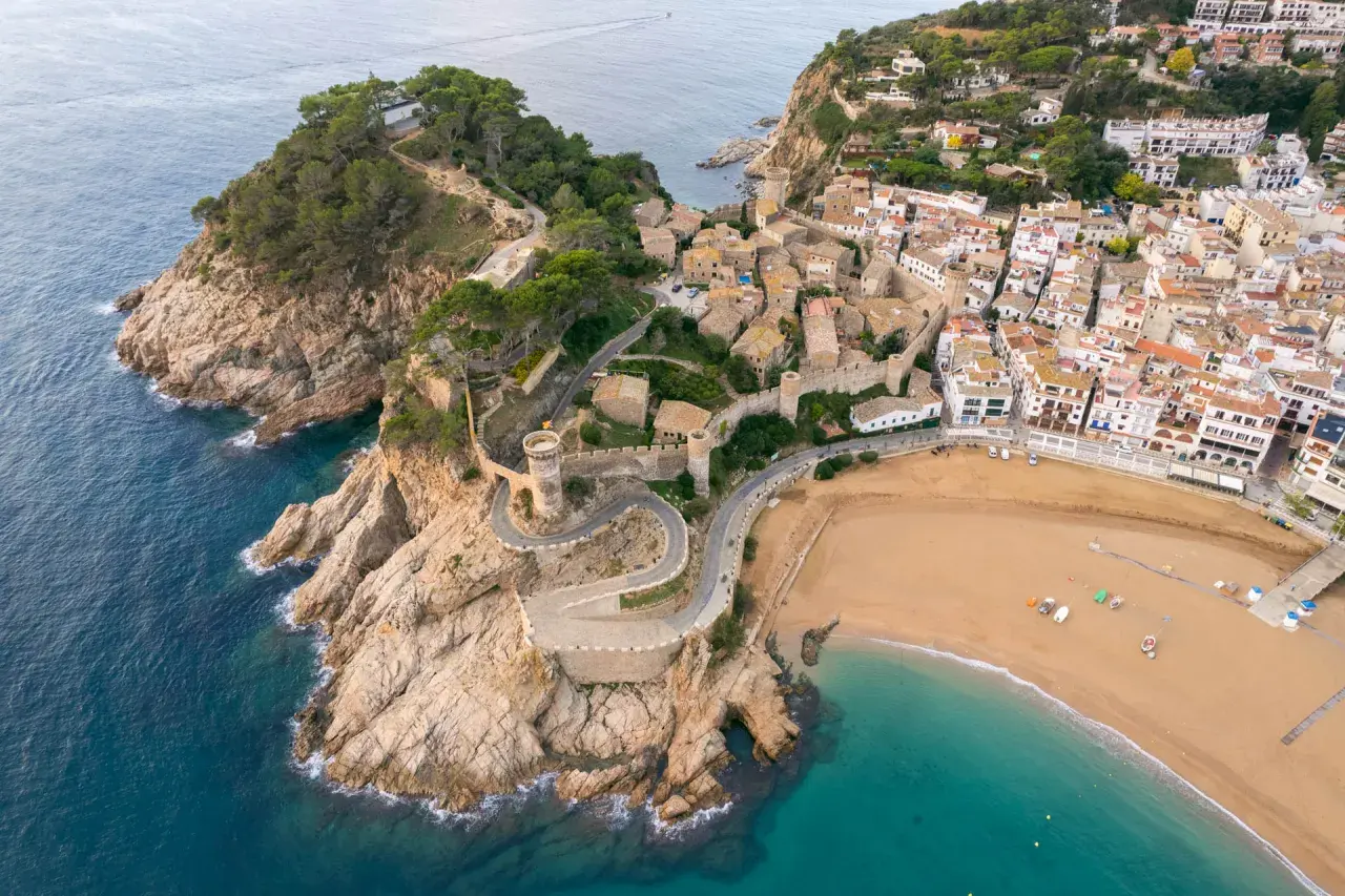 Malownicze widoki na Costa Brava wakacje: miasteczko z zamkiem na klifie, kręta droga i piaszczysta plaża.