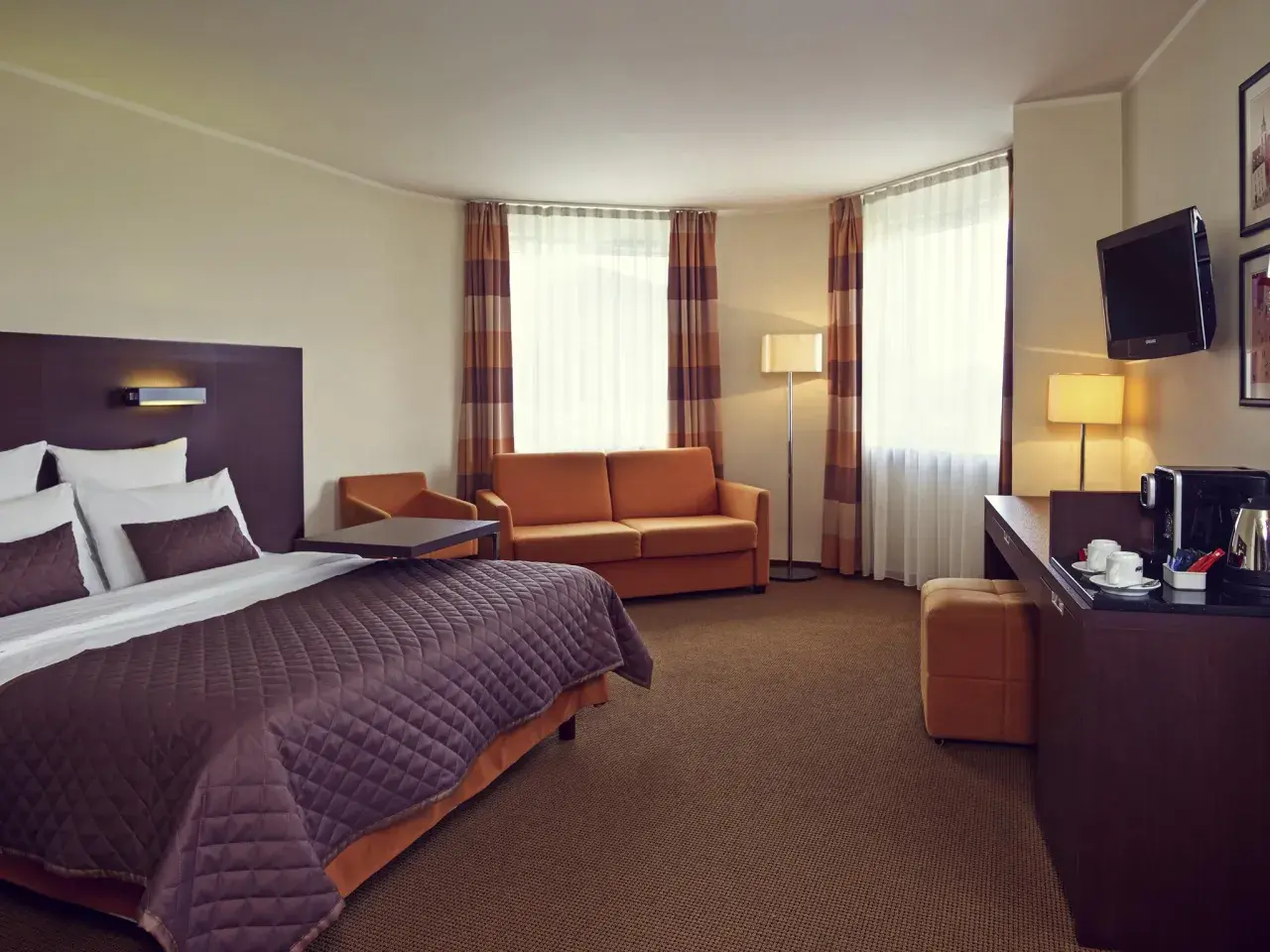 Przytulny pokój w hotelu Mercure Warszawa Airport: łóżko, kanapa, biurko z ekspresem do kawy i TV.
