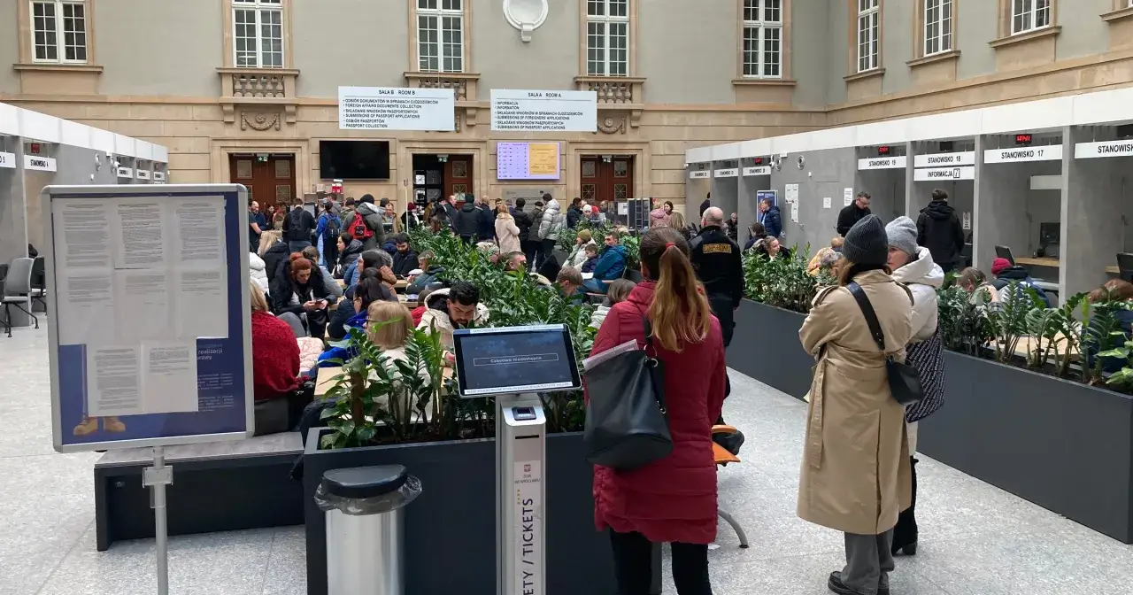 Tłum ludzi czeka na paszport w urzędzie. Widać stanowiska obsługi i tablice informacyjne.