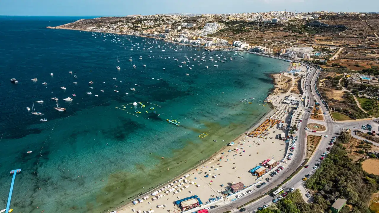 Malta jest bezpieczna, plaża pełna ludzi i łodzi, turkusowa woda zaprasza do kąpieli.
