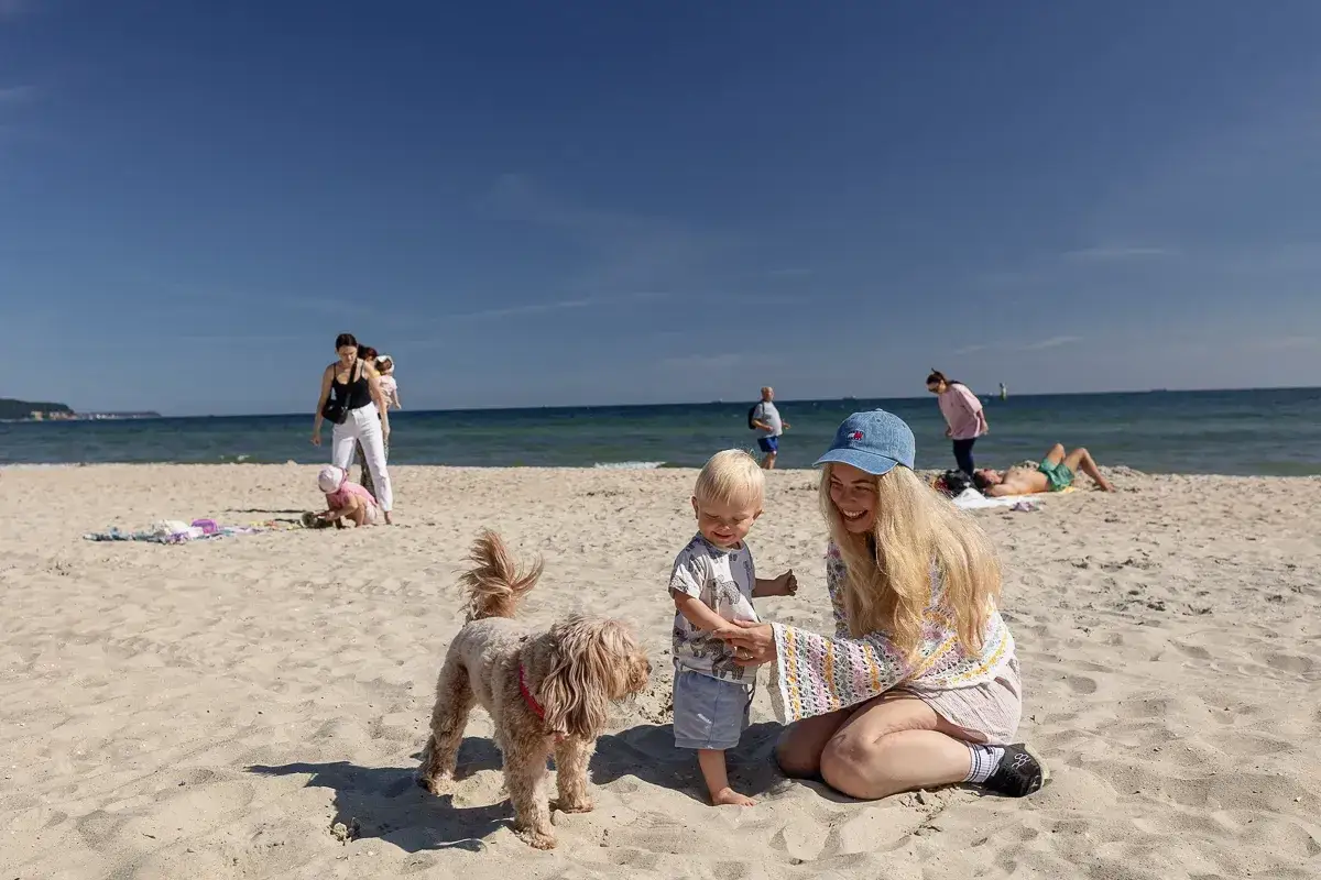 Radosne wakacje z niemowlakiem na plaży. Kobieta z dzieckiem i psem cieszą się słońcem.
