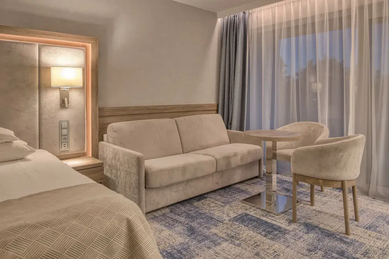 Wygodna sofa i fotele w pokoju hotelowym 5 gwiazdkowym. Miękkie oświetlenie, elegancka pościel i nowoczesny dywan tworzą przytulną atmosferę.