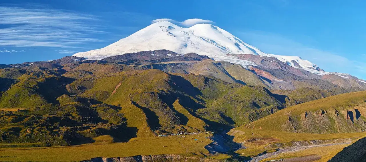 Majestatyczny, ośnieżony najwyższy szczyt Kaukazu, Elbrus, góruje nad zielonymi, pofałdowanymi zboczami.