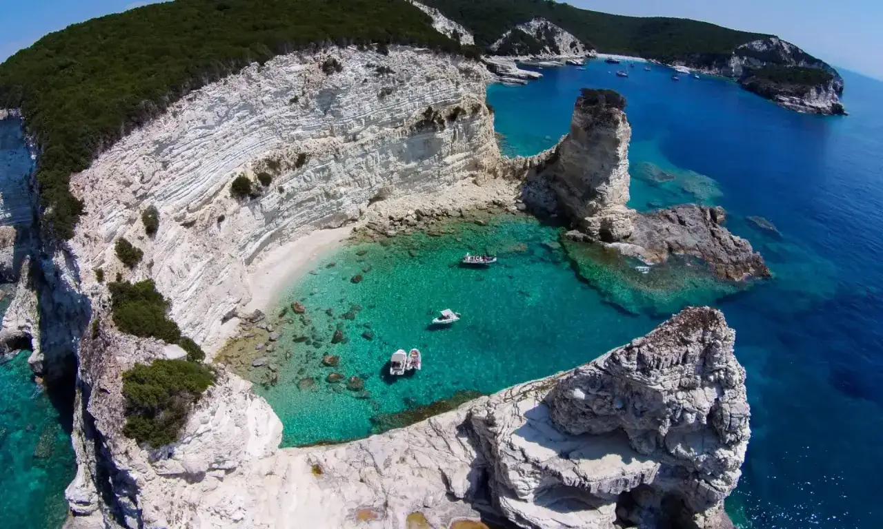 Turkusowe zatoczki i białe klify Paxos i Antipaxos, z łodziami cumującymi w krystalicznie czystej wodzie.
