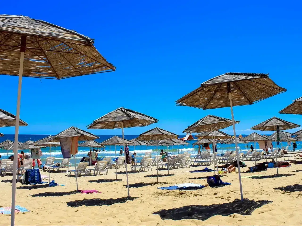 Słoneczna plaża w Bułgarii, pełna leżaków i parasoli. Ludzie odpoczywają, ciesząc się słońcem. Czy w Bułgarii jest bezpiecznie? Tak, to popularny kierunek wakacyjny.
