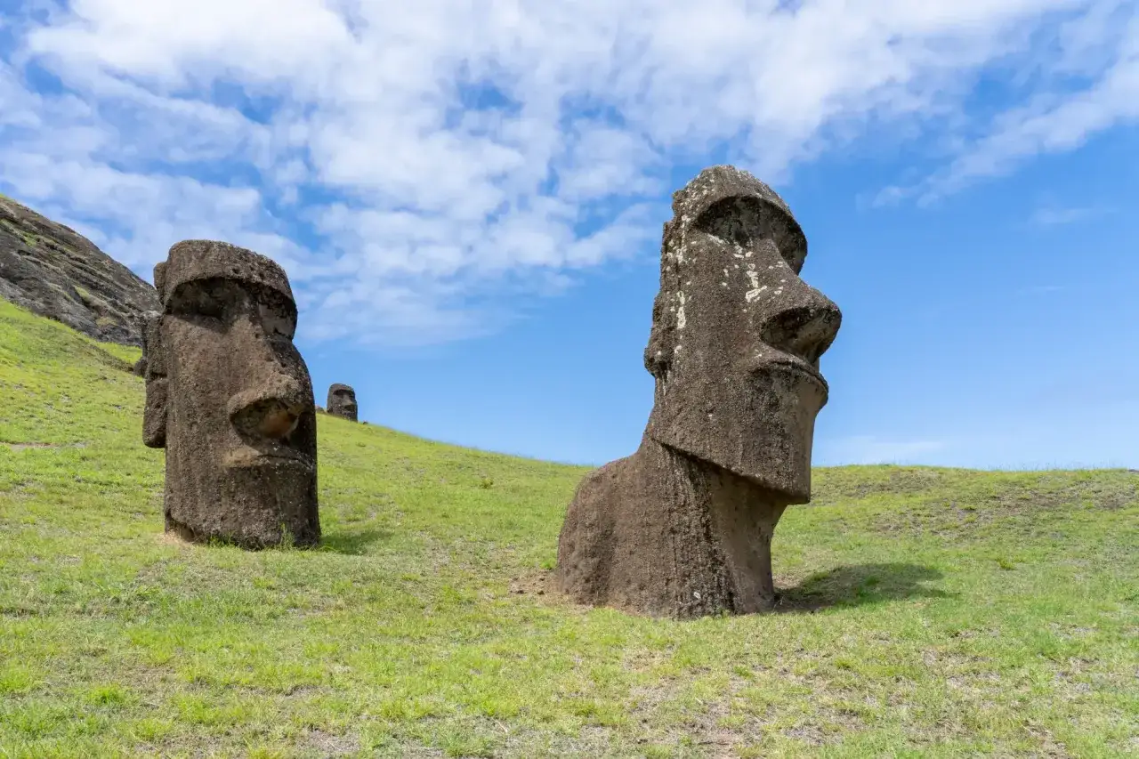 Kamienne moai na zielonym wzgórzu pod błękitnym niebem.
