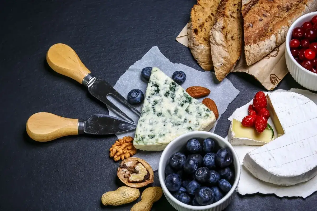 Wykwintne francuskie jedzenie: sery pleśniowe i camembert, bagietka, jagody, żurawina, orzechy i migdały.