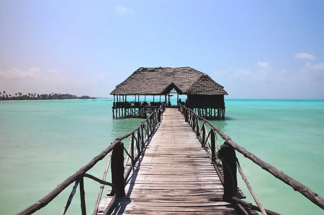 Drewniany pomost prowadzi do chatki na palach w turkusowej wodzie. Idealne miejsce na wiza zanzibar.